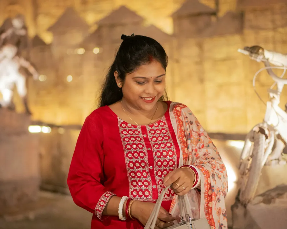 A smiling woman in an embroidered red kurta looking into a white handbag